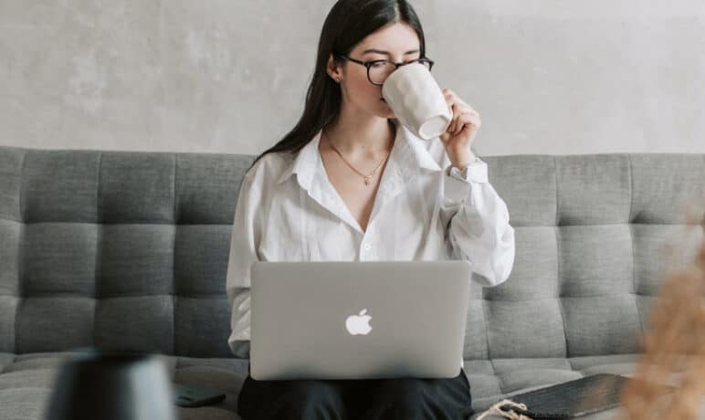 vrouw zittend op bank met laptop op schoot. Mok aan de mond