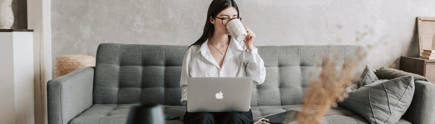 vrouw zittend op bank met laptop op schoot. Mok aan de mond