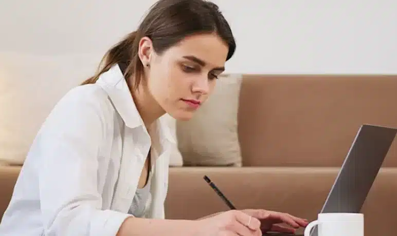 vrouw aan koffietafel aan het schrijven, laptop en kopje op tafel