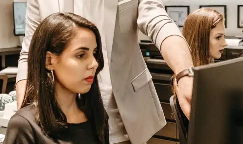 vrouw zittend voor computer, man die achter haar staat en wijst naar het scherm