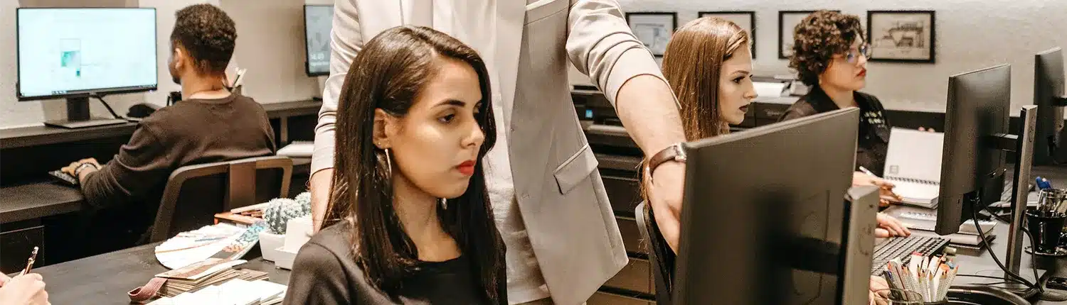 vrouw zittend voor computer, man die achter haar staat en wijst naar het scherm
