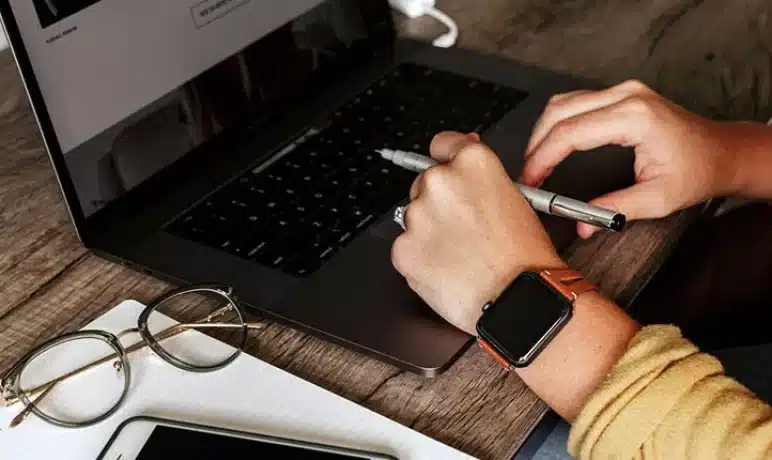 handen die pen vasthouden boven toetsenbord van laptop.