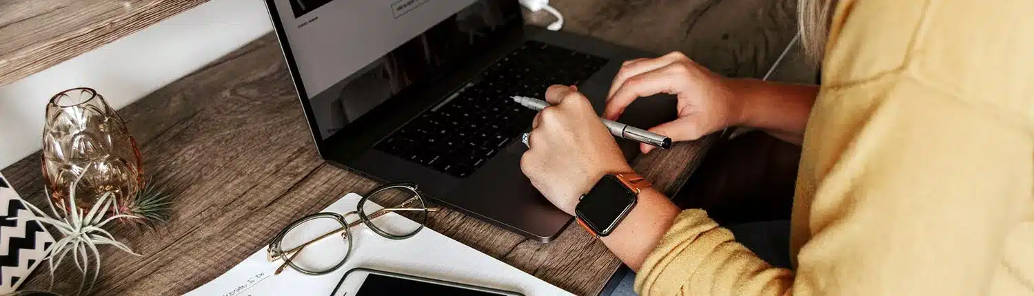 handen die pen vasthouden boven toetsenbord van laptop.